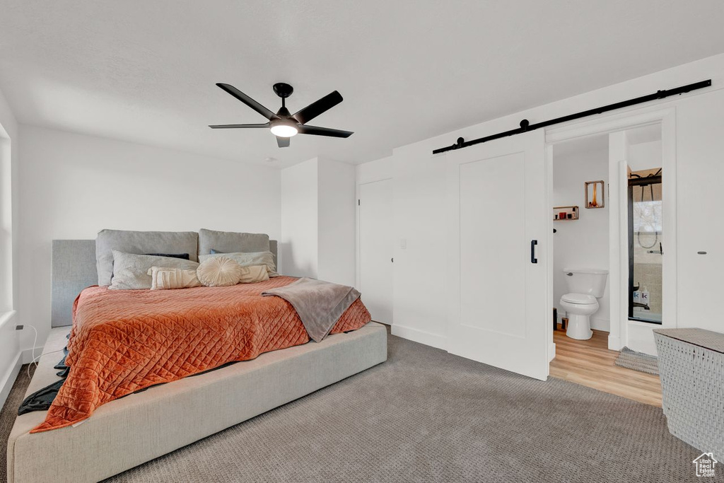 Bedroom featuring a barn door, connected bathroom, light hardwood / wood-style floors, and ceiling fan