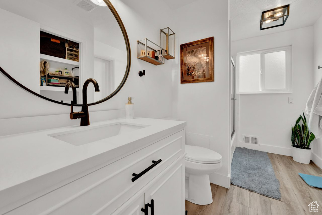 Full bathroom with enclosed tub / shower combo, toilet, large vanity, and hardwood / wood-style flooring