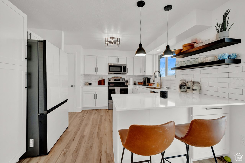 Kitchen featuring decorative light fixtures, backsplash, a kitchen breakfast bar, light hardwood / wood-style floors, and stainless steel appliances