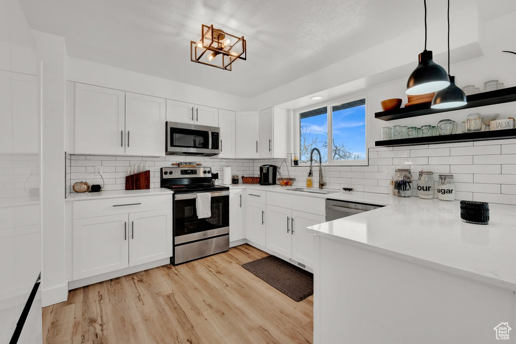 Kitchen featuring decorative light fixtures, appliances with stainless steel finishes, white cabinets, light wood-type flooring, and sink