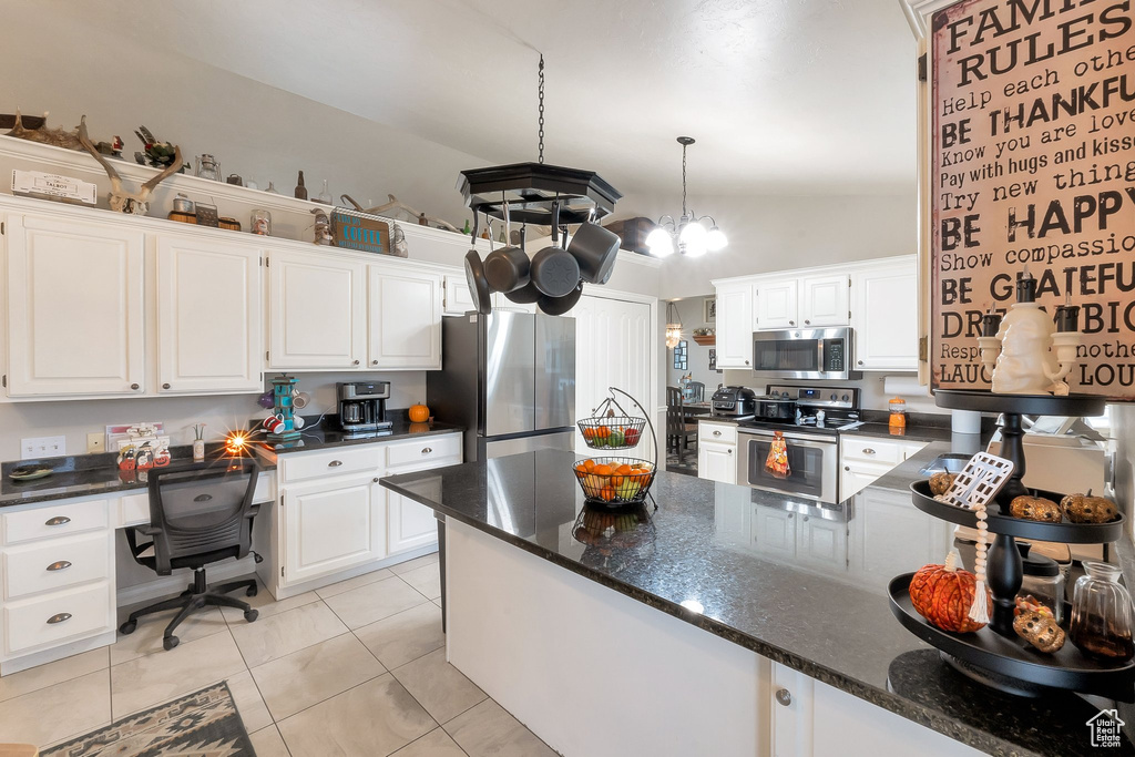Kitchen featuring decorative light fixtures, vaulted ceiling, appliances with stainless steel finishes, white cabinets, and an inviting chandelier