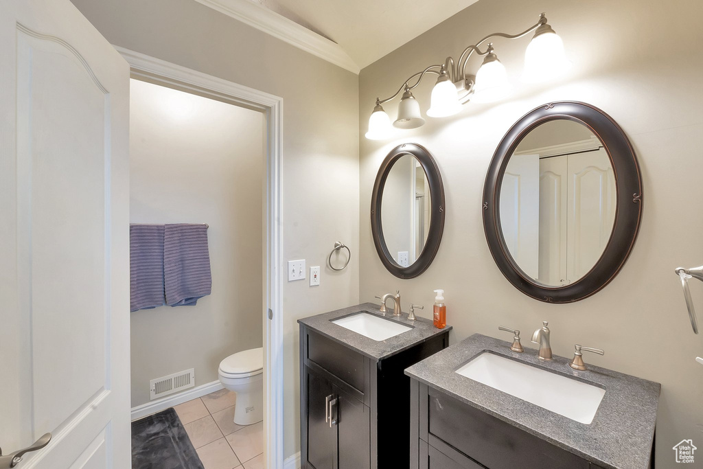 Bathroom featuring toilet, double sink vanity, ornamental molding, lofted ceiling, and tile floors