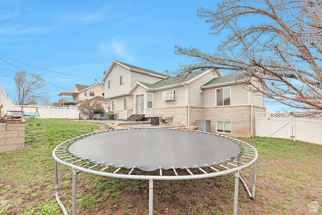 Back of house with a trampoline and a yard