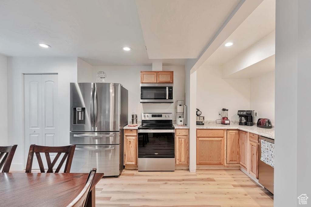 Kitchen featuring light brown cabinets, stainless steel appliances, light stone countertops, and light wood-type flooring