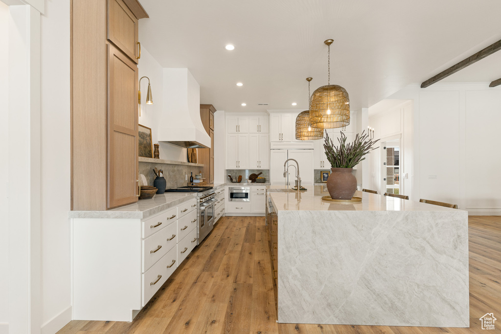Kitchen with light hardwood / wood-style floors, an island with sink, hanging light fixtures, and white cabinets