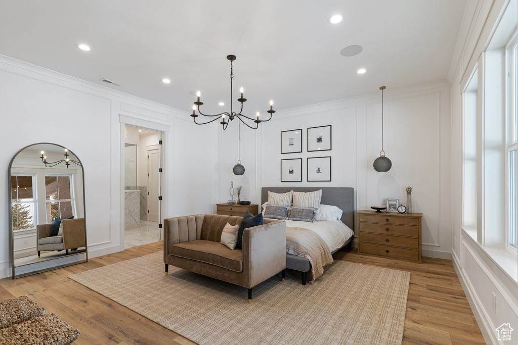 Bedroom with ornamental molding, ensuite bath, a notable chandelier, and light wood-type flooring