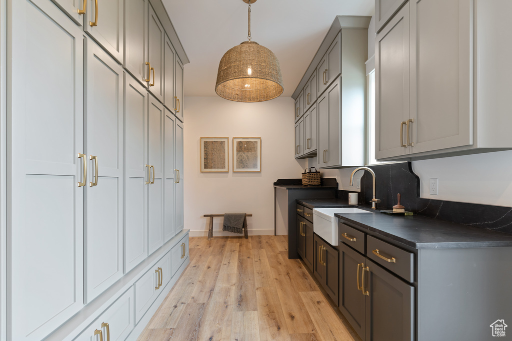 Kitchen with gray cabinetry, light hardwood / wood-style floors, pendant lighting, and sink