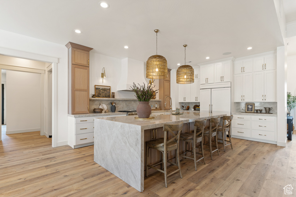 Kitchen with white cabinetry, backsplash, light hardwood / wood-style floors, and an island with sink