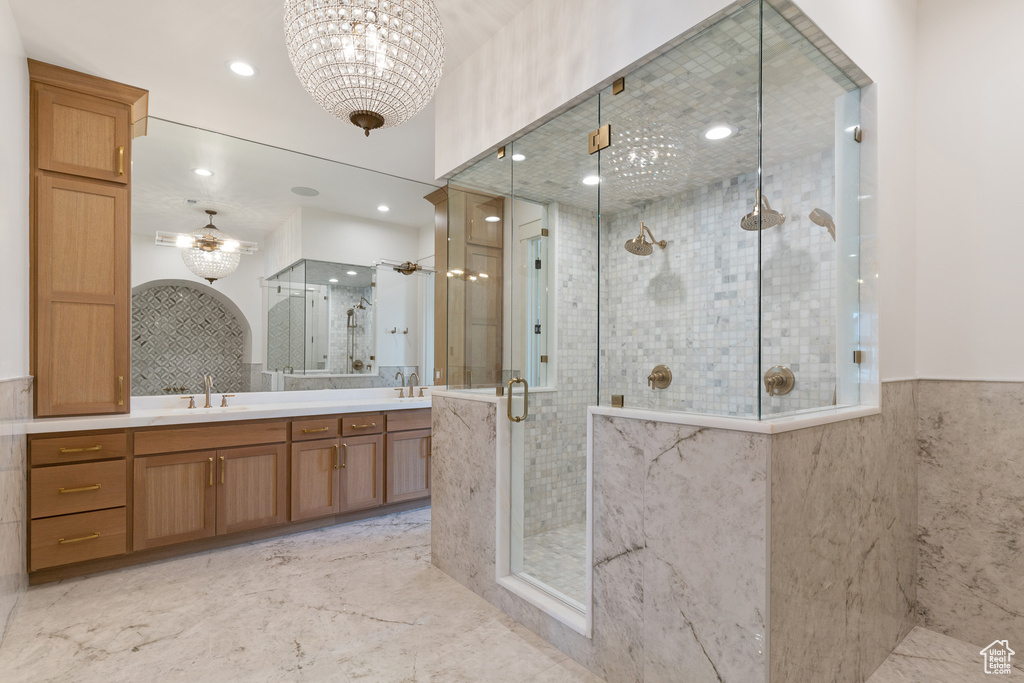 Bathroom featuring double sink, ceiling fan with notable chandelier, tile floors, vanity with extensive cabinet space, and a shower with shower door
