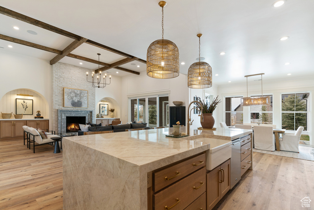 Kitchen with pendant lighting, light hardwood / wood-style floors, a fireplace, a kitchen island with sink, and dishwasher