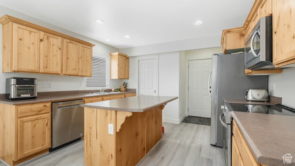 Kitchen with appliances with stainless steel finishes, a kitchen island, sink, and light wood-type flooring