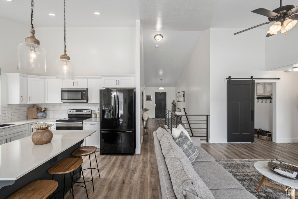 Kitchen featuring ceiling fan, a barn door, a kitchen bar, light wood-type flooring, and stainless steel appliances