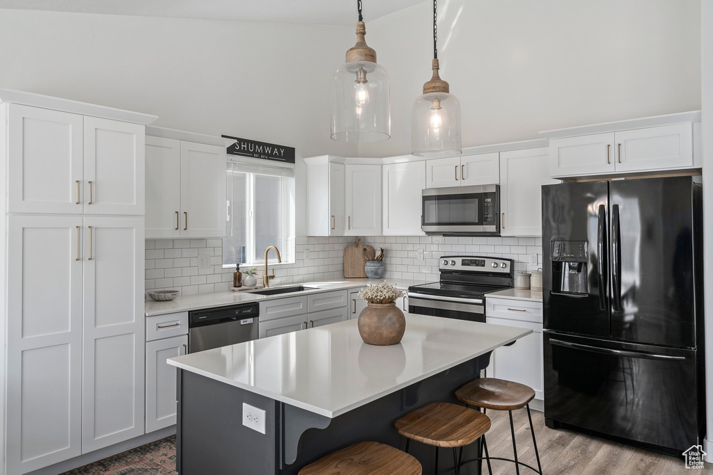 Kitchen featuring light hardwood / wood-style floors, a kitchen island, a kitchen bar, appliances with stainless steel finishes, and sink