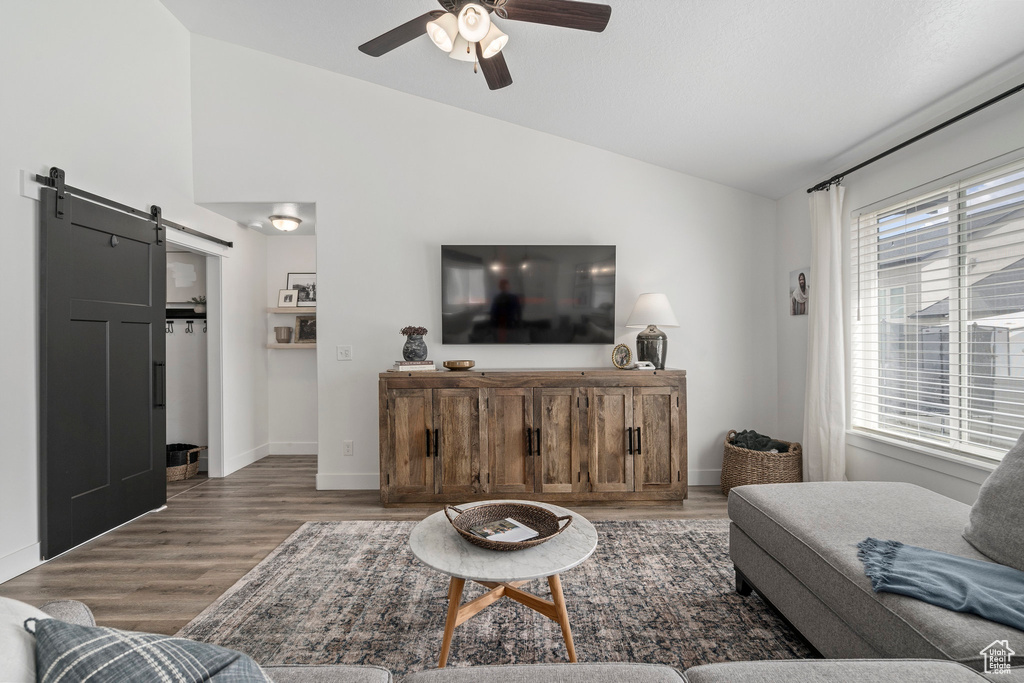Living room featuring a barn door, ceiling fan, dark hardwood / wood-style floors, and lofted ceiling
