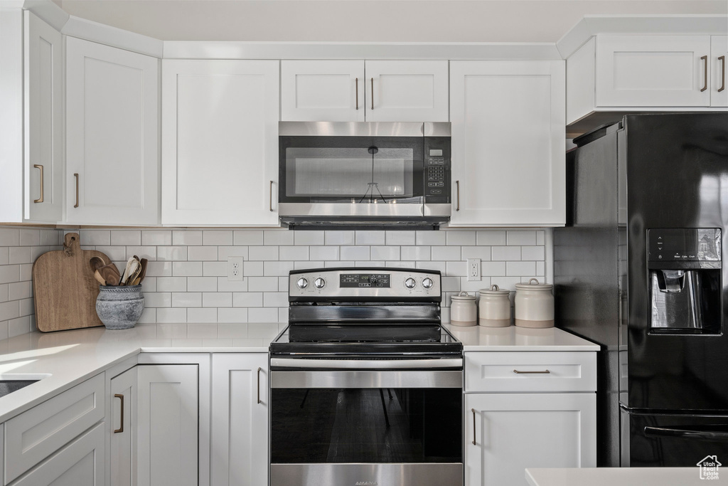 Kitchen with backsplash, appliances with stainless steel finishes, and white cabinetry