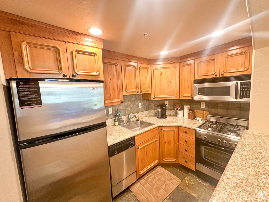 Kitchen with sink, stainless steel appliances, dark tile flooring, and tasteful backsplash