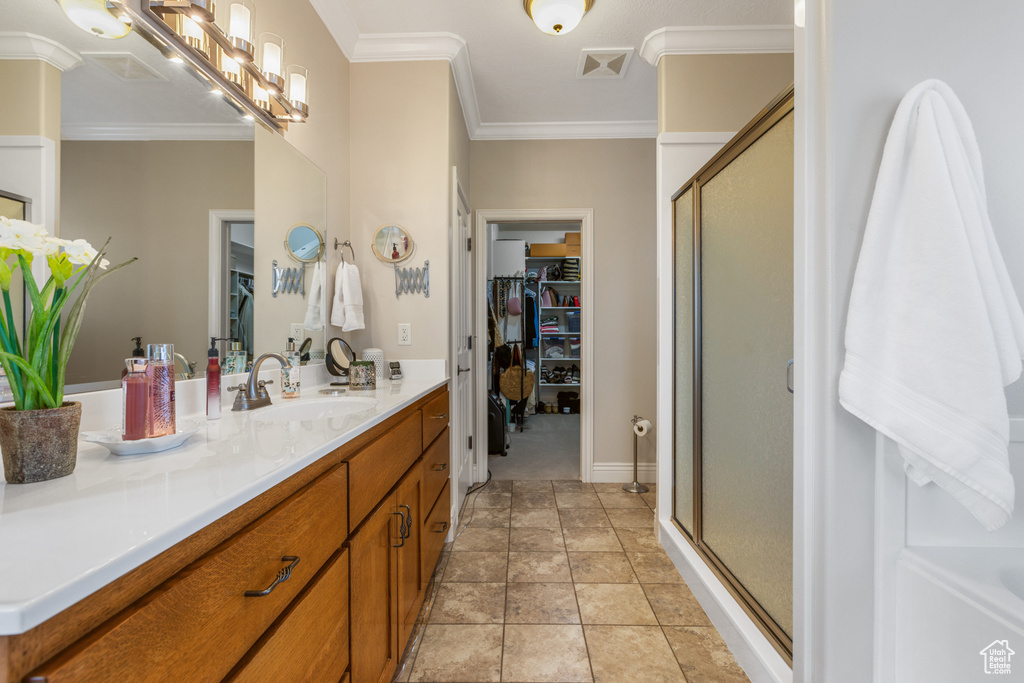 Bathroom with vanity with extensive cabinet space, ornamental molding, tile floors, and a shower with door