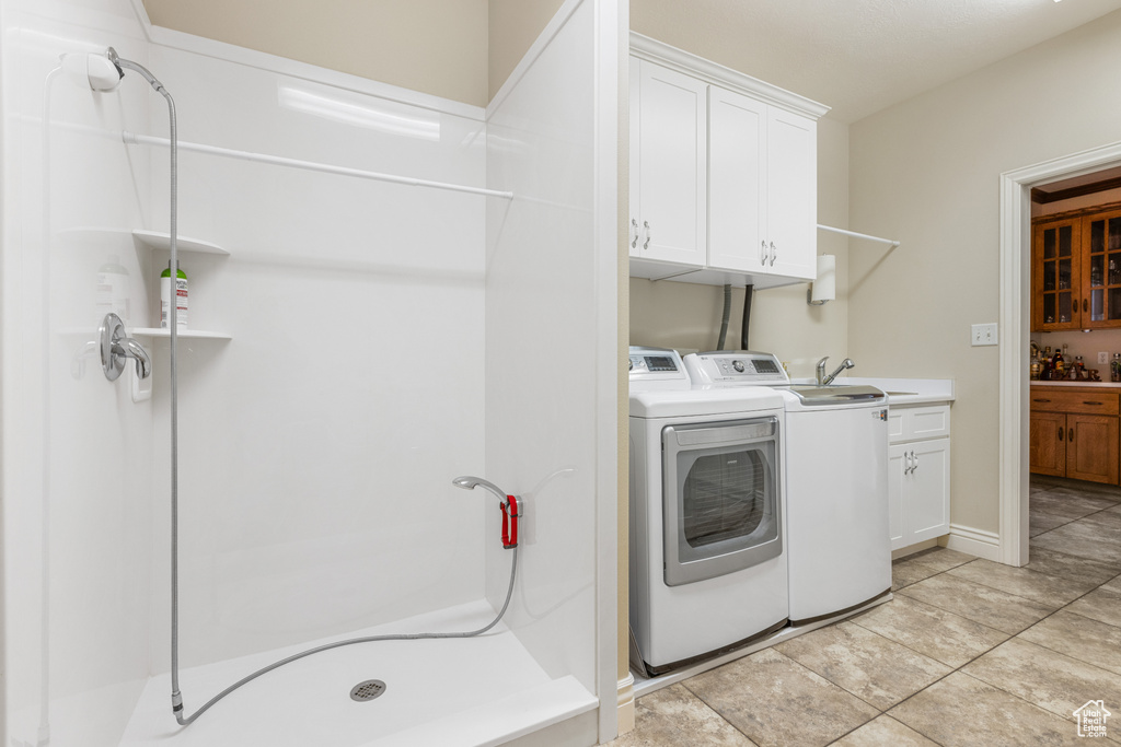 Laundry area with independent washer and dryer, light tile floors, cabinets, and sink