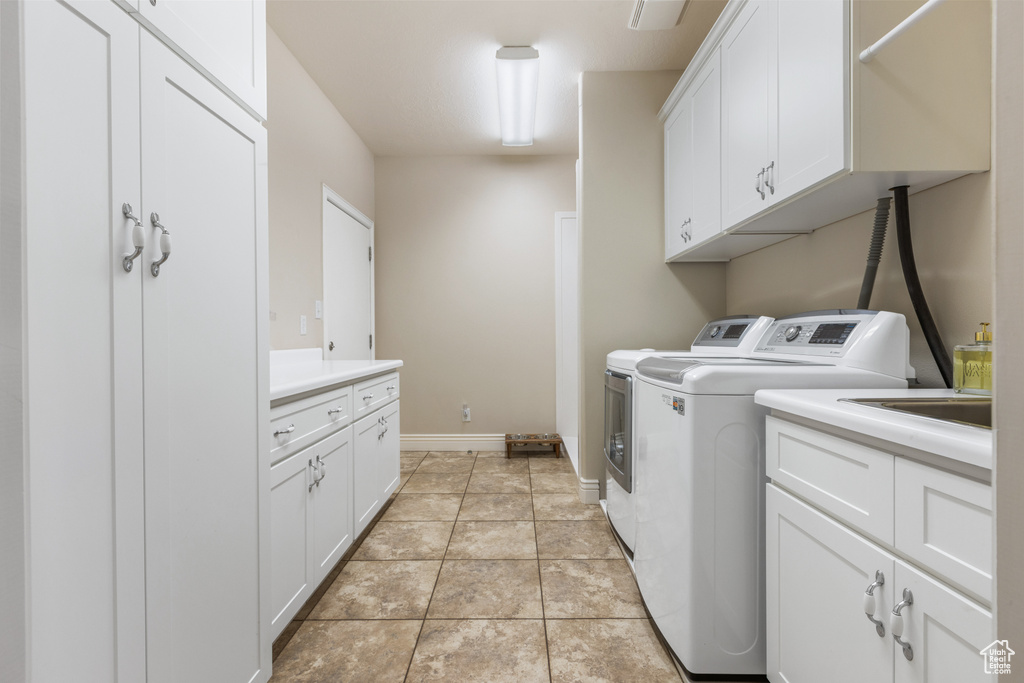 Clothes washing area with cabinets, washing machine and clothes dryer, and light tile flooring