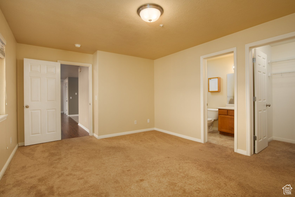 Unfurnished bedroom featuring a spacious closet, dark colored carpet, and ensuite bathroom