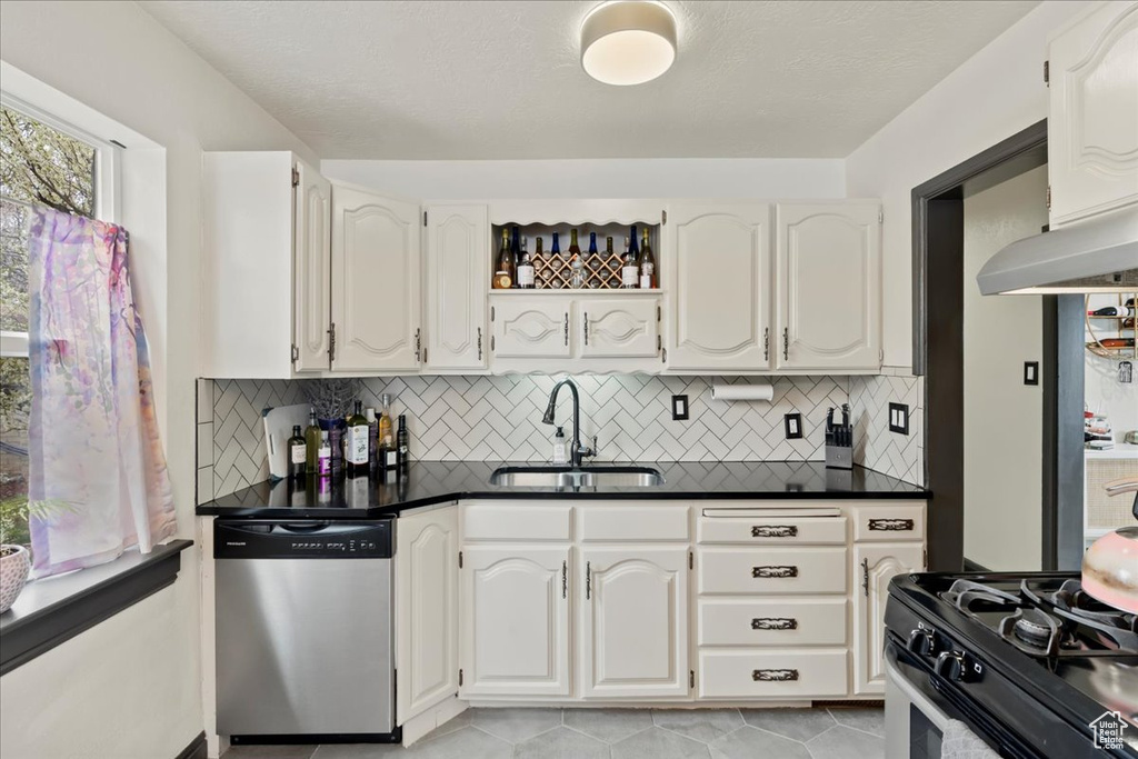 Kitchen with white cabinetry, stainless steel dishwasher, sink, and light tile flooring