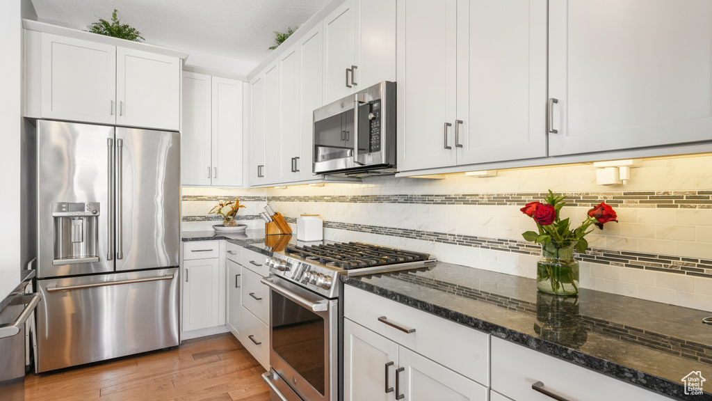Kitchen featuring high quality appliances, light hardwood / wood-style floors, tasteful backsplash, white cabinetry, and dark stone countertops