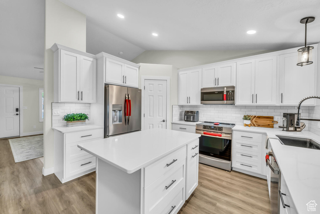 Kitchen featuring pendant lighting, light hardwood / wood-style floors, lofted ceiling, and stainless steel appliances