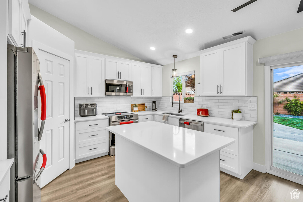 Kitchen featuring hanging light fixtures, white cabinets, appliances with stainless steel finishes, light hardwood / wood-style flooring, and lofted ceiling