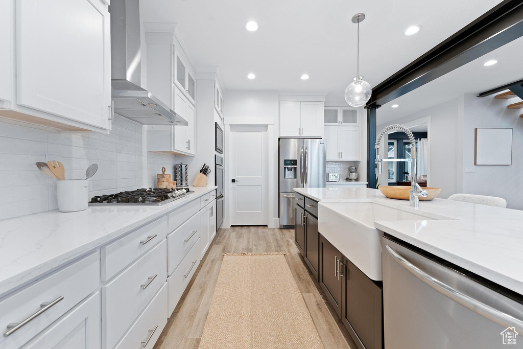 Kitchen with white cabinets, tasteful backsplash, and wall chimney range hood