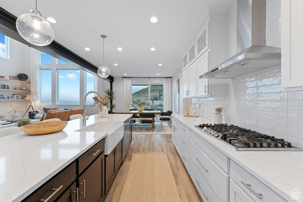 Kitchen featuring pendant lighting, dark brown cabinets, appliances with stainless steel finishes, wall chimney range hood, and tasteful backsplash