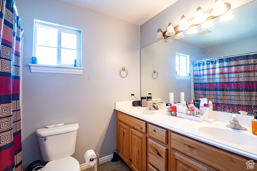 Bathroom featuring toilet, tile floors, double sink, and vanity with extensive cabinet space