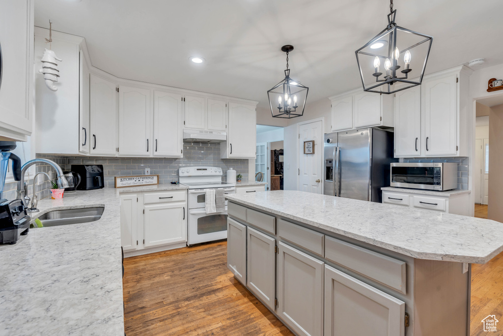 Kitchen with light hardwood / wood-style floors, white electric range oven, stainless steel fridge, backsplash, and hanging light fixtures