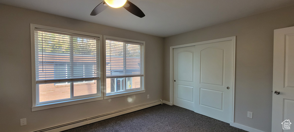 Unfurnished bedroom with a closet, ceiling fan, a baseboard radiator, and multiple windows