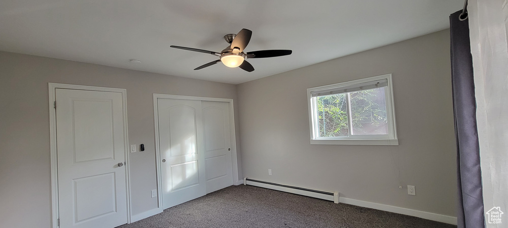 Unfurnished bedroom featuring dark colored carpet, a baseboard radiator, and ceiling fan