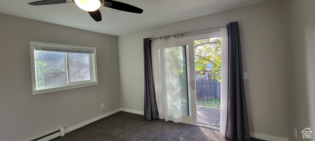 Spare room with a baseboard heating unit, ceiling fan, dark carpet, and a wealth of natural light