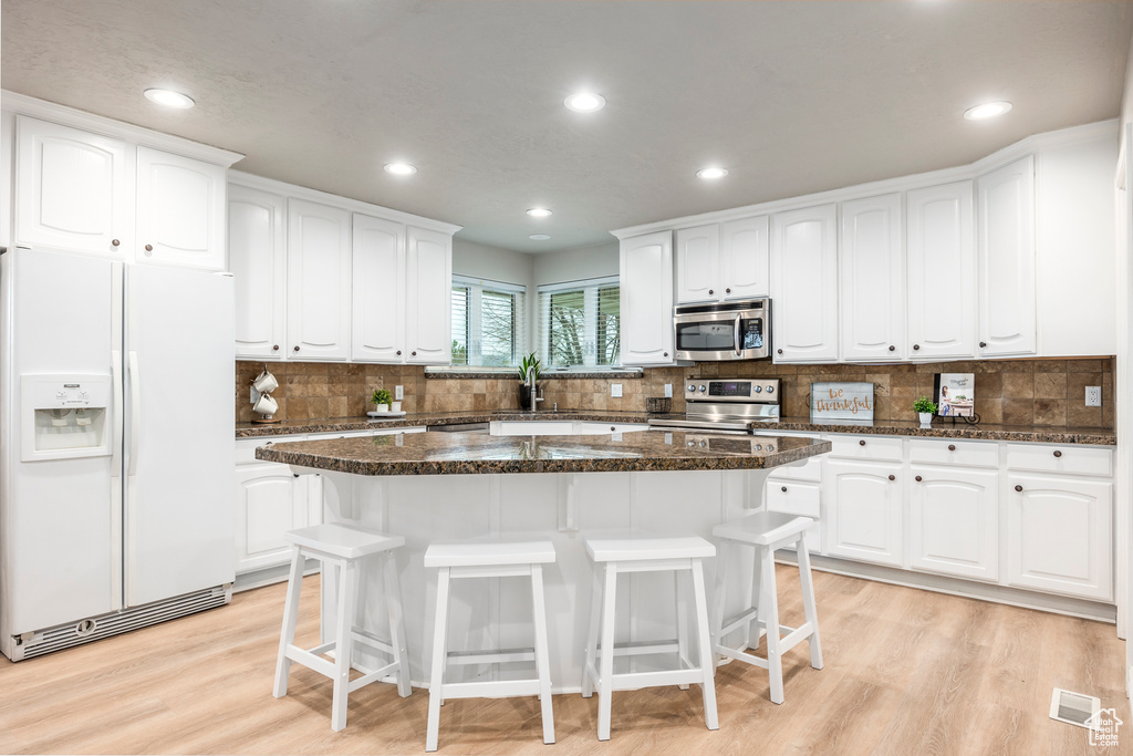 Kitchen featuring a kitchen island, stainless steel appliances, a kitchen breakfast bar, and light wood-type flooring