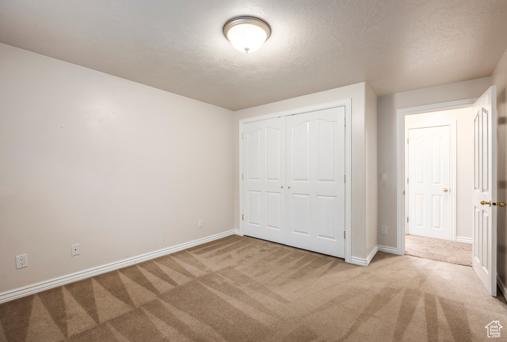 Unfurnished bedroom with a closet, a textured ceiling, and light colored carpet