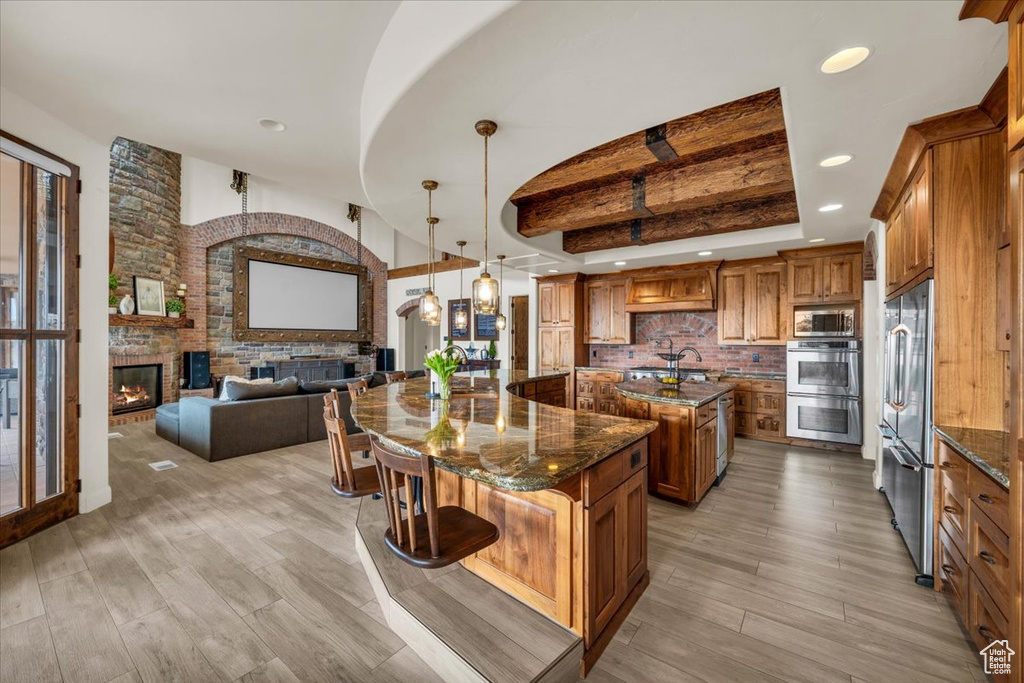 Kitchen with light hardwood / wood-style floors, decorative light fixtures, a fireplace, a center island with sink, and backsplash