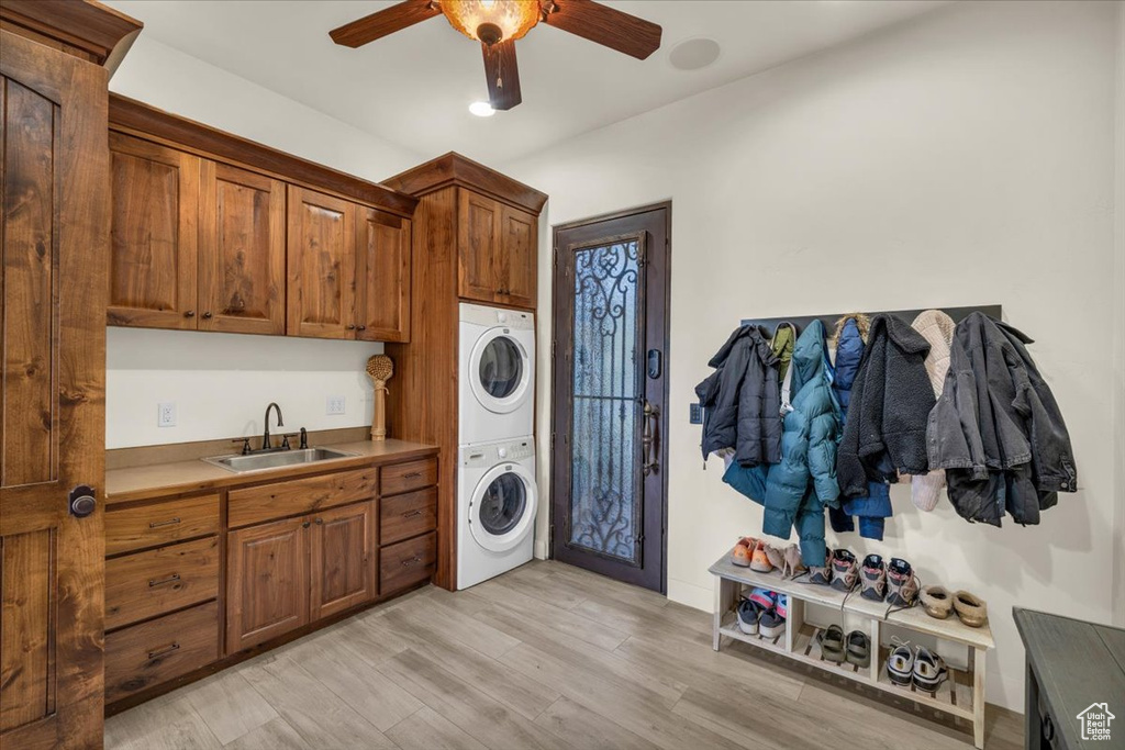 Laundry room featuring ceiling fan, stacked washer / drying machine, cabinets, sink, and light hardwood / wood-style flooring