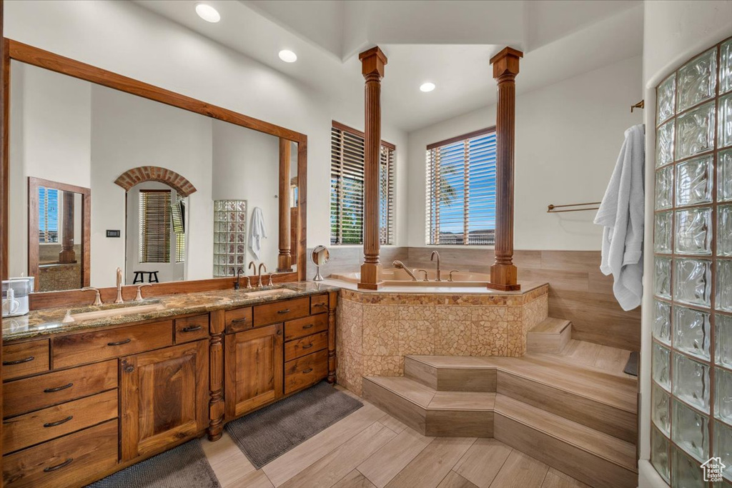 Bathroom featuring dual vanity, tiled tub, and ornate columns