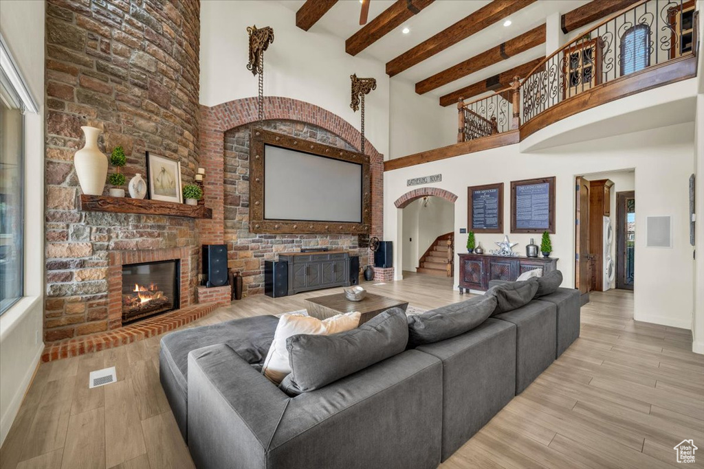 Living room with light hardwood / wood-style floors, a stone fireplace, and a towering ceiling