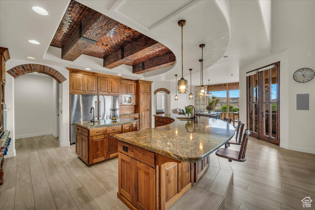Kitchen with beamed ceiling, light hardwood / wood-style flooring, a large island, hanging light fixtures, and light stone counters