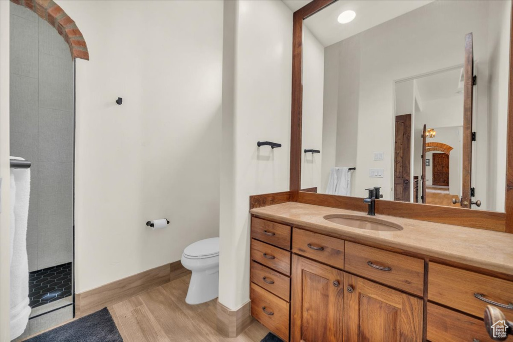 Bathroom featuring hardwood / wood-style flooring, toilet, vanity, and tiled shower
