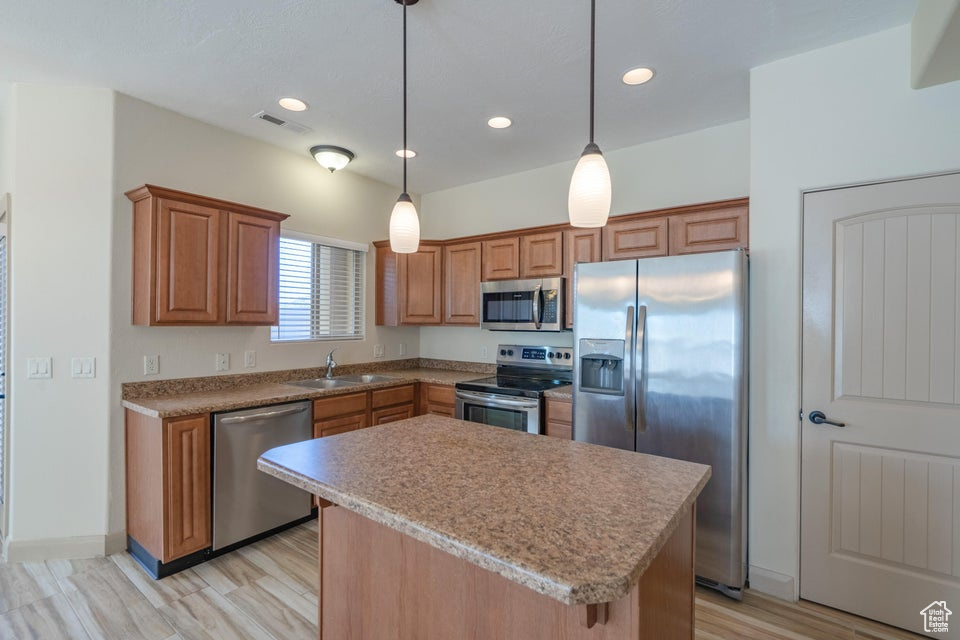 Kitchen with sink, appliances with stainless steel finishes, light hardwood / wood-style floors, decorative light fixtures, and a center island