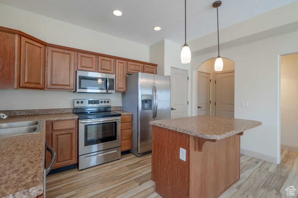 Kitchen with decorative light fixtures, appliances with stainless steel finishes, sink, light hardwood / wood-style flooring, and a kitchen island