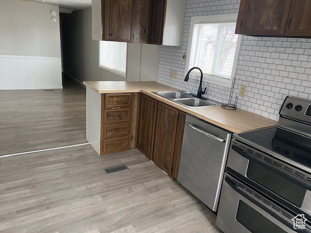 Kitchen featuring sink, light hardwood / wood-style flooring, stainless steel appliances, tasteful backsplash, and dark brown cabinetry