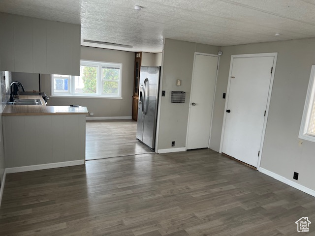 Kitchen with kitchen peninsula, a textured ceiling, sink, stainless steel fridge, and dark hardwood / wood-style flooring