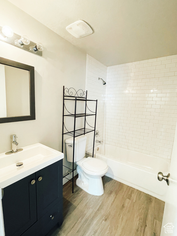 Full bathroom with tiled shower / bath, toilet, hardwood / wood-style floors, and vanity