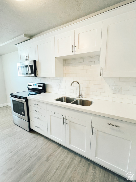 Kitchen featuring sink, light hardwood / wood-style flooring, stainless steel appliances, tasteful backsplash, and white cabinetry