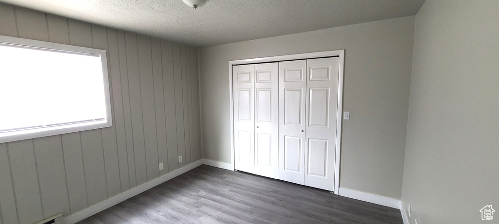 Unfurnished bedroom with a textured ceiling, a closet, multiple windows, and hardwood / wood-style flooring
